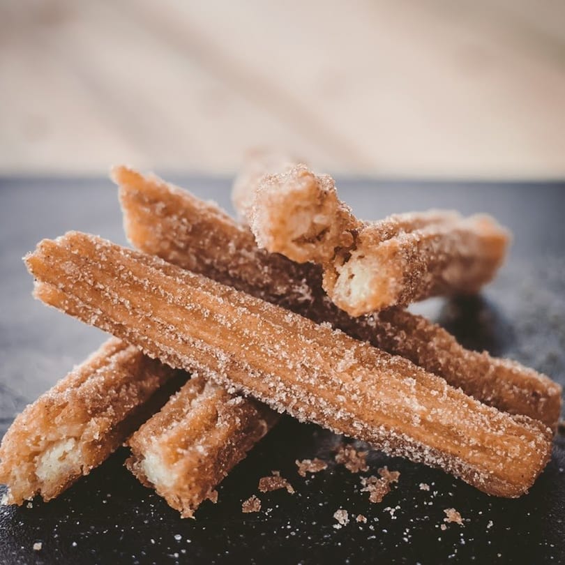 A close-up of several churros, golden brown and coated in sugar, on a dark surface.