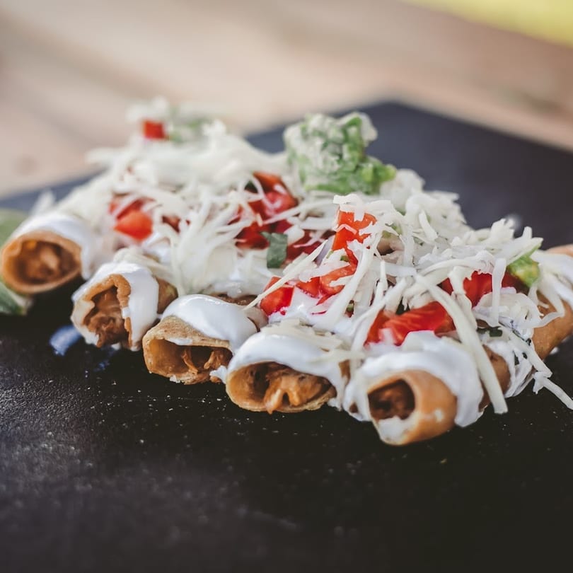 Crispy taquitos from Azul Tacos, topped with shredded cabbage, diced tomatoes, and crema.