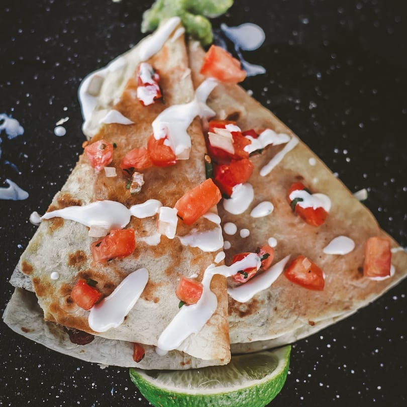 Two quesadilla wedges topped with diced tomatoes, sour cream, and a lime wedge on a dark surface.